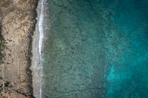 Vibrant coastal landscape showing the clear blue waters meeting the rocky shore at midday