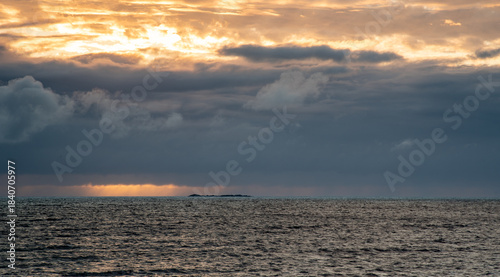 Beautiful sunset over the ocean with dramatic clouds and distant land on the horizon,