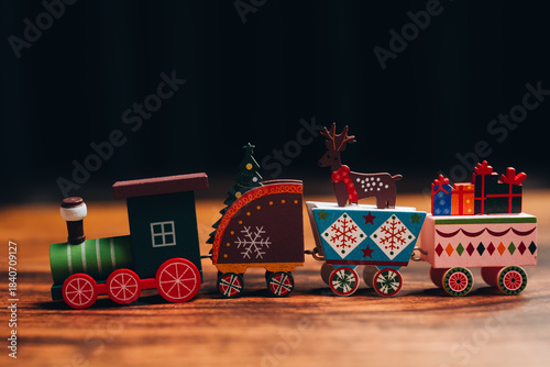 Christmas concept. Wooden toy train with Christmas decorations including reindeer, tree, and gift boxes on wooden surface with dark background, festive holiday spirit