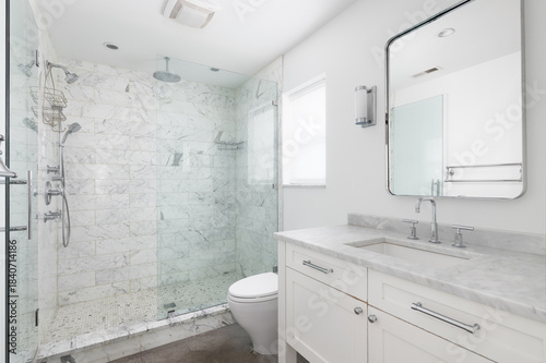 A bright and modern white bathroom featuring a spacious glass-enclosed shower with marble tile and a white vanity with a marble countertop.