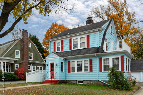 Charming two-story family home with blue siding and red shutters surrounded by autumn foliage in Brighton, Boston, Massachusetts, USA
