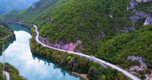 Aerial view of bus driving on winding mountain road beside river