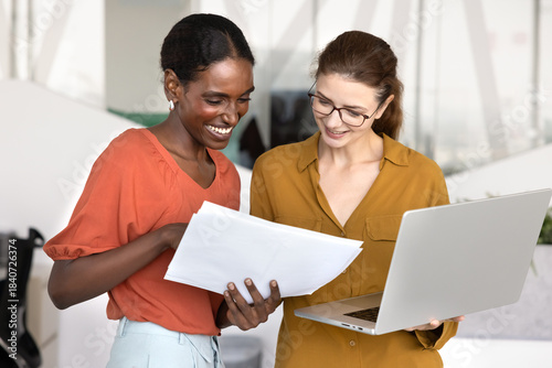 Happy young African American professional woman consulting financial or legal expert briefly, showing paper report to coworker, pointing at document, asking for advice, assistance, consultation