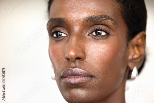 Face of young African American woman with naturally smooth skin, minimal makeup, curled eyelashes, well-shaped lips. Black female model looking away, posing for close up natural beauty portrait