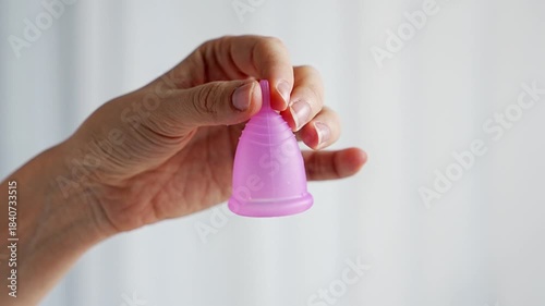 Close-up of a pink menstrual cup standing upright on a woman open palm over wooden table. Feminine hygiene product promoting zero waste, comfort, and sustainable period care.