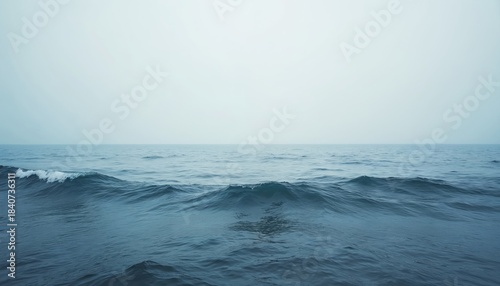 Calm sea surface with small waves and horizon. Gentle ocean water rolls towards shore under pale sky. Natural tranquil seascape reflects peace.