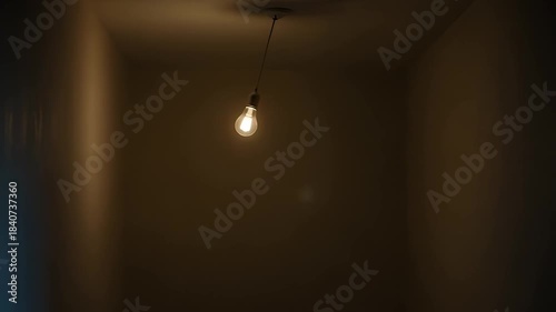 Single lightbulb swings gently in an empty room with bare walls and dim lighting