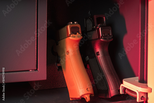 Modern handguns, one black and one tan, stored securely in a dimly lit gun safe, emphasizing firearm safety and home protection.