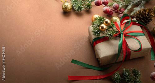 Christmas banner background with handmade craft gift box with bow, decorative fir branch, balls for tree decoraton. New Year winter holiday composition with presents, decor and copy space for text.