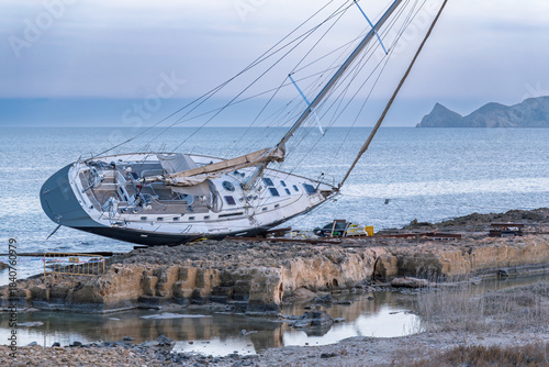 Javea Alicante 10 12 2025 – A stranded sailboat resting on the rocky coastline of Javea, Spain, with clear Mediterranean waters and dramatic shore scenery.