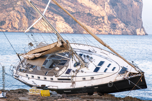 Javea Alicante 10 12 2025 – A stranded sailboat resting on the rocky coastline of Javea, Spain, with clear Mediterranean waters and dramatic shore scenery.