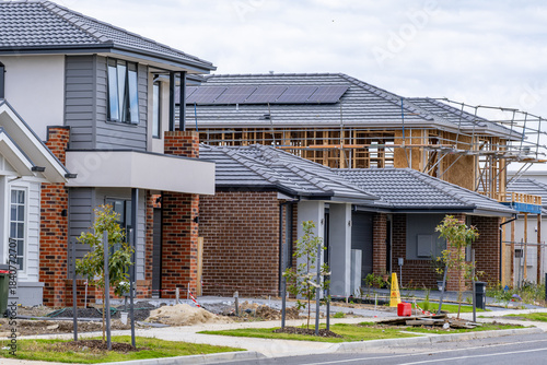 New estate housing development in suburban Melbourne, showing completed modern homes alongside an active construction site with timber framing and roofing works. Housing boom, urban expansion