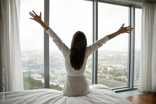Meeting beautiful morning. Rear view happy overjoyed young lady in nightgown sitting on bed stretch hands with pleasure open arms to new day looking toward glass wall window with marvelous cityscape Free Download Meeting beautiful morning. Rear view happy overjoyed young lady in nightgown sitting on bed stretch hands with pleasure open arms to new day looking toward glass wall window with marvelous cityscape - GFXLoad