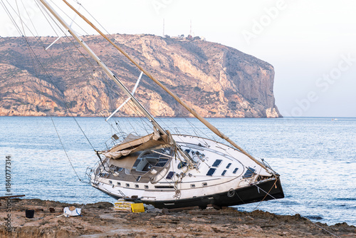 Javea Alicante 10 12 2025 – A stranded sailboat resting on the rocky coastline of Javea, Spain, with clear Mediterranean waters and dramatic shore scenery.