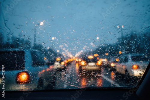 Holiday traffic jam on rainy evening with blurred car lights seen through wet windshield creating moody urban atmosphere and reflecting city life challenges
