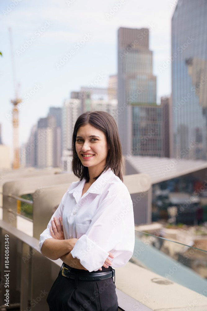 Fototapeta premium Smiling woman standing on a rooftop balcony overlooking the city.