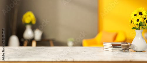 Fototapeta Naklejka Na Ścianę i Meble -  Sunflower vase with book and coffee cup on marble counter table across yellow sofa in grey wall room