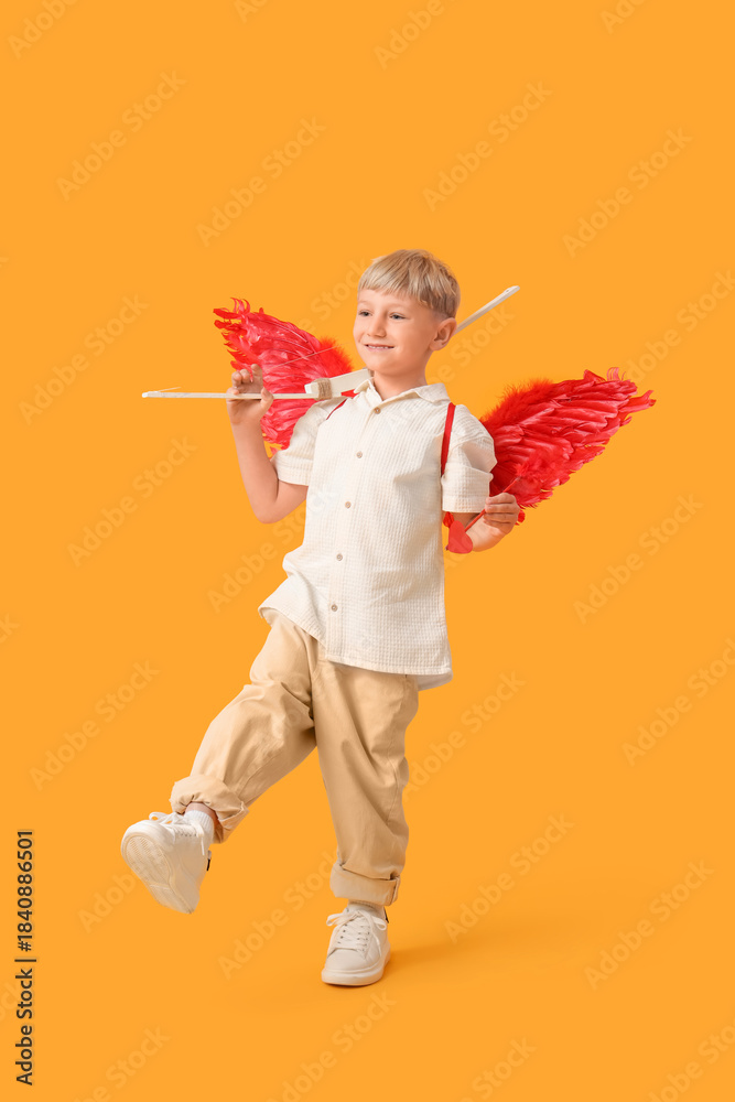 Naklejka premium Cute little happy boy dressed as cupid with bow and arrow on yellow background. Valentine's Day celebration