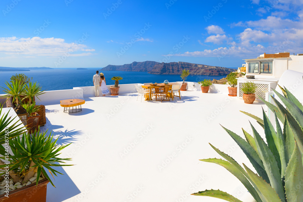 Fototapeta premium An attractive young couple stands together on a whitewashed terrace overlooking the sea and caldera at Oia, Greece, on the island of Santorini.