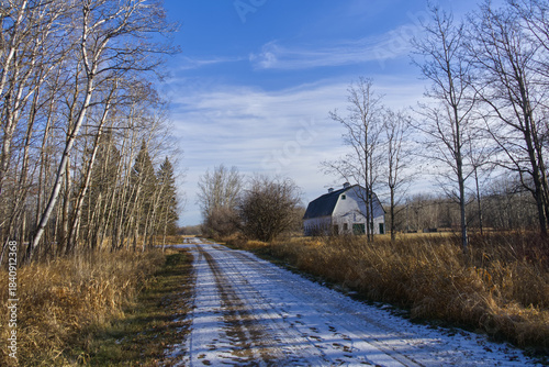Snow on a dirt road with a Barn at the side
