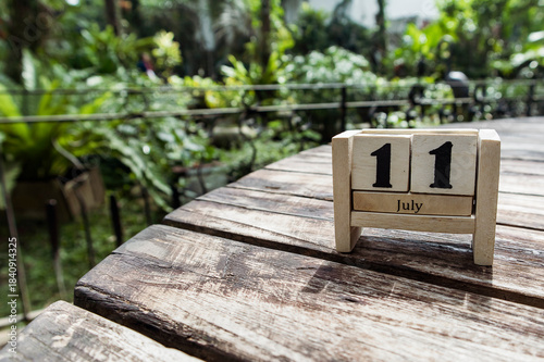 Wooden cube calendar for 11th July place on a table in a sunny garden background