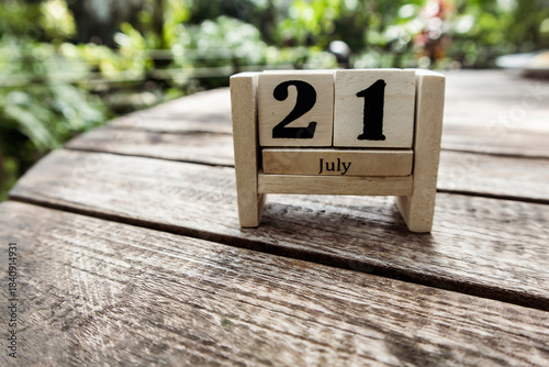 Wooden cube calendar for 21st July place on a table in a sunny garden background
