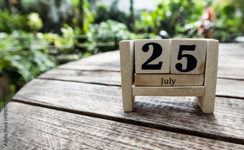 Wooden cube calendar for 25th July place on a table in a sunny garden background