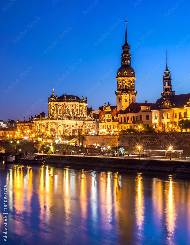 Obraz premium Dresden cityscape at night with illuminated buildings reflecting in the Elbe River, showcasing historic German architecture under a vibrant blue sky.