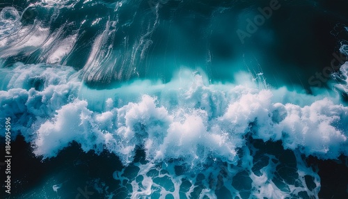 This abstract aerial view captures a powerful deep turquoise ocean wave dramatically crashing, revealing high-contrast white foam crests.