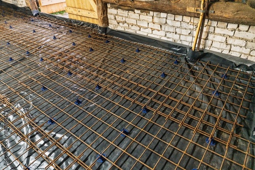 Foto A construction site displays a reinforcement grid elevated by blue supports on a black membrane, prepared for a concrete slab pour, ensuring structural integrity and durability