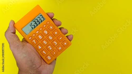 Fotografi Close-up on an orange pocket calculator held in a hand, set against a cheerful yellow backdrop