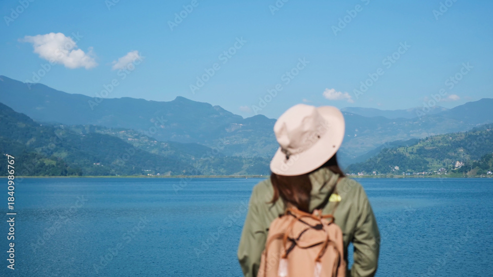 Fototapeta premium Blurred rear view image of a woman looking at a beautiful mountains and the Phewa lake in Pokhara, Nepal