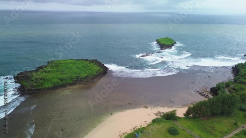 Aerial footage of a pristine and stunningly beautiful beach area. Drone footage captures the beach, featuring expansive green grass, pristine white sand, and a small island just off the mainland.
