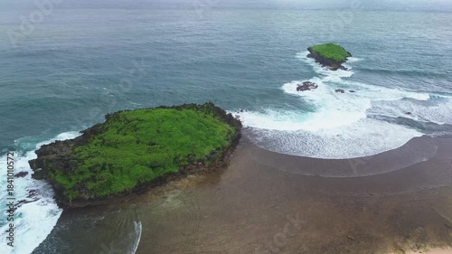Aerial footage of a pristine and stunningly beautiful beach area. Drone footage captures the beach, featuring expansive green grass, pristine white sand, and a small island just off the mainland.