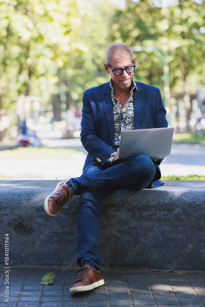Obraz premium Mature man working remote on laptop in park