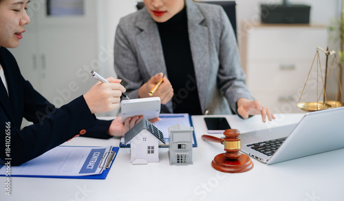Real estate agent discussing property contract with client, showing house model, agreement, and legal consultation for home buying and investment.
