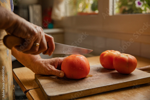 Φωτογραφία A woman's hands cutting a tomato into wedges on a cutting board