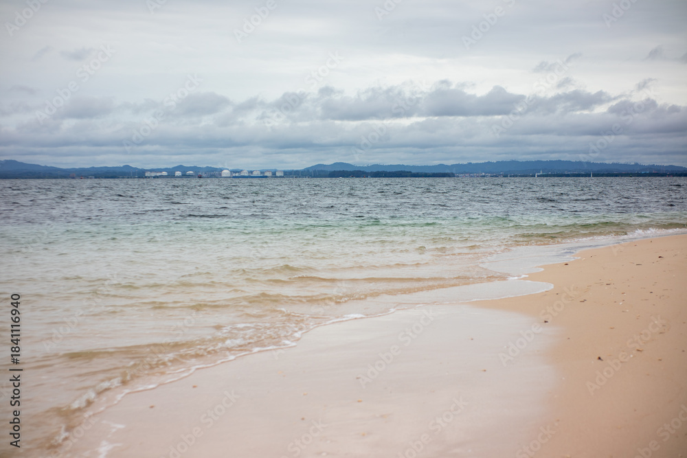 Fototapeta premium Tranquil Coastal Scene of Sand and Ocean Under Overcast Tropical Sky