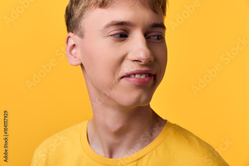 Fotografía Sour expression on a teenage male wearing a yellow shirt against a bright yellow backdrop, capturing a candid moment of discomfort or hesitation with a playful mood