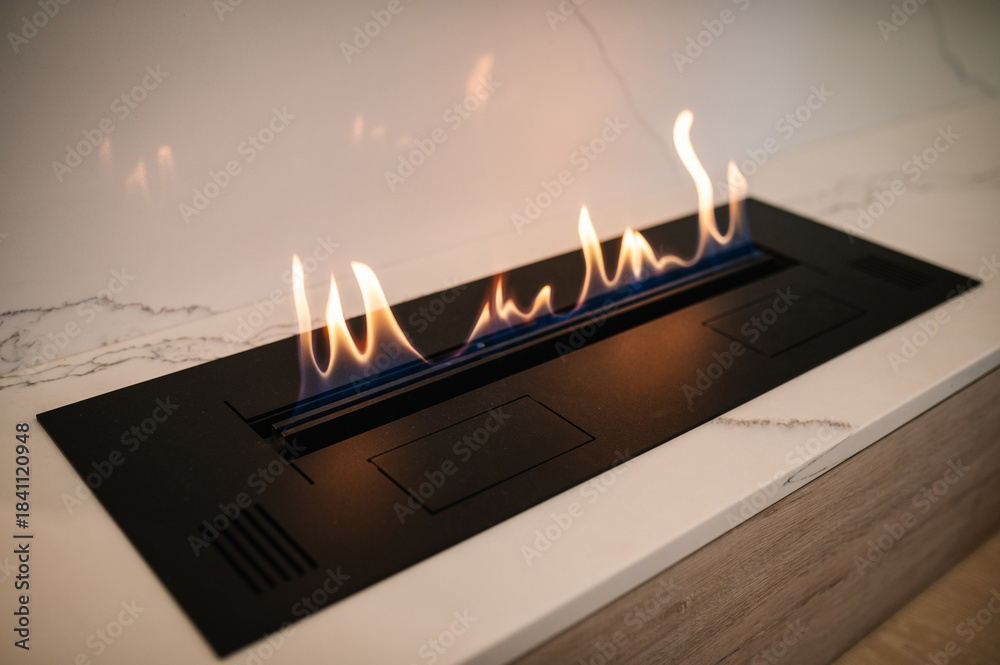 Obraz premium Burning eco bio ethanol fireplace built into white marble. Automatic tabletop biofireplace. Beautiful marble fireplace. Minimalist interior, alternative bio fireplot fireplace on ethanol gas.