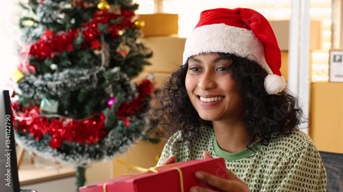 Small business warehouse, Christmas season with female staff offering festive gift, presenting holiday package with cheerful expression and supporting ecommerce order preparation in seasonal workspace