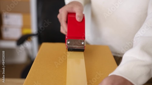 Warehouse shipping workflow showing young worker attaching label to parcel, preparing delivery orders, managing ecommerce packing process, supporting logistics operation in small business storehouse