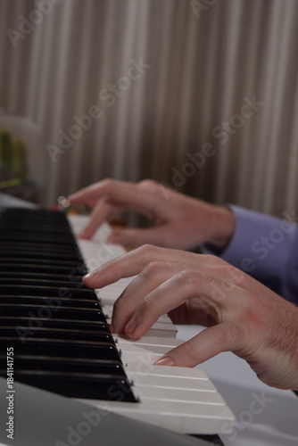 A young white man plays an electronic synthesizer indoors, immersed in his creative hobby. Focused on shaping tones and melodies, he explores musical expression and artistry in a calm home setting.
