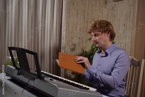 A young white man plays an electronic synthesizer indoors, immersed in his creative hobby. Focused on shaping tones and melodies, he explores musical expression and artistry in a calm home setting.
