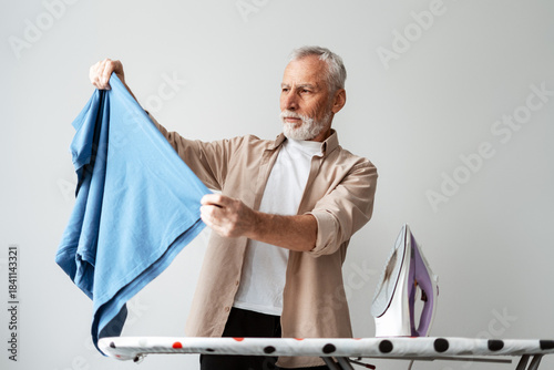 Φωτογραφία Senior man inspecting blue shirt before ironing, focused on household chores
