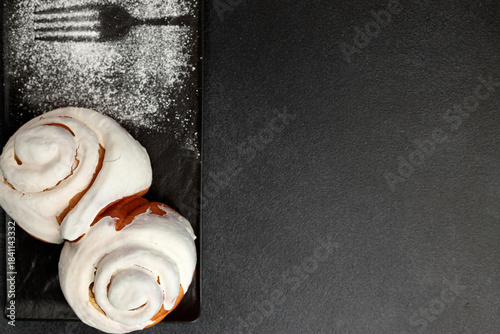 Fragrant cinnabons with cream on a black rectangular plate on a gray background
