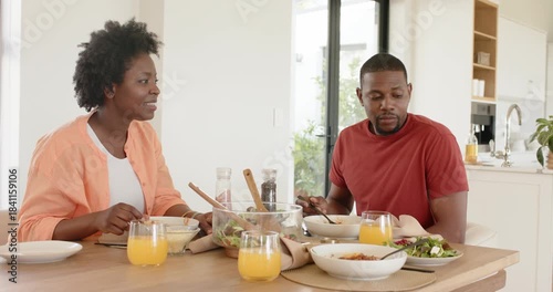 African American family eating from cereal bowls at dining table when mother beckoning son for hug