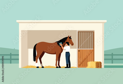 A person grooms a brown horse in a stable. A bale of hay and a fence are also visible