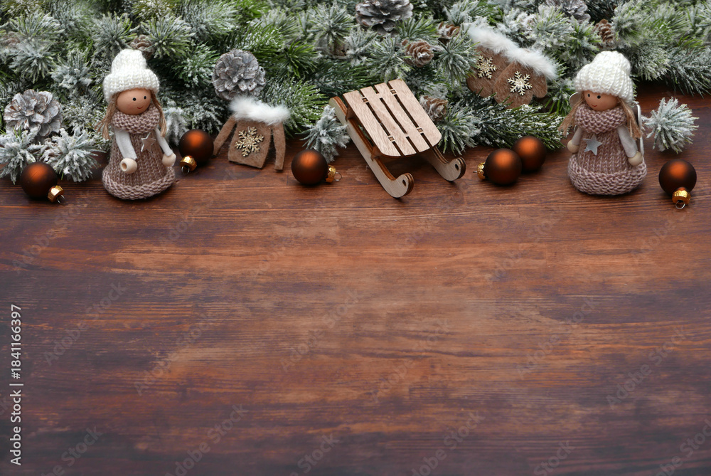 Obraz premium Christmas background: Christmas scene with small dolls, sleds, fir branches and Christmas decorations on a wooden background with space for text.