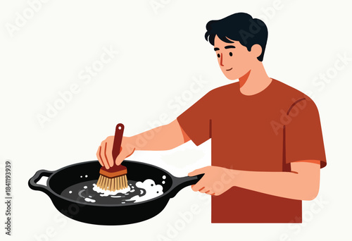 A person, in a terracotta shirt, cleans a cast-iron skillet with soap and a brush. The background is white